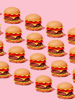 A plastic toy hamburger pattern covers a minimalist pink background