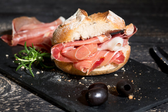 Parma ham, rolls and black olives on dark wood