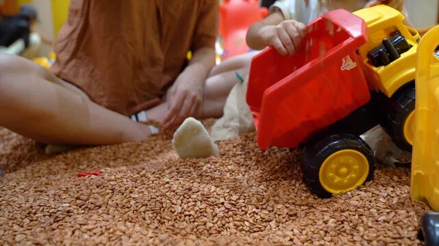 Children playing with toy dump truck in indoor sensory grain play area