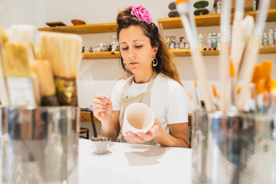 Artisan woman paints a handmade ceramic mug in her workshop