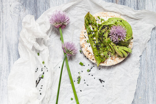 Rice cakes with cream cheese, avocado and asparagus garnished with black cumin seeds and chive blossom