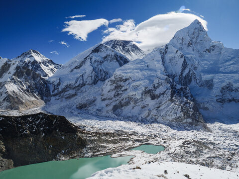 Panoramic view of Mount Everest and surrounding Himalayan peaks with a glacial lake and icefall under a clear blue sky in Nepal.