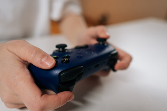 Close-up of female gamer hands adjusting modern navy blue wireless video game controller, preparing for online multiplayer gaming, leisure activity, digital fun on sitting at white table.