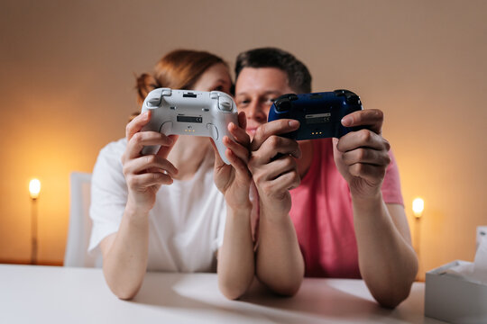 Front view of happy young couple enjoying home entertainment, holding wireless video game controllers, bonding over competitive or cooperative gameplay, having fun together, leisure activity at home.