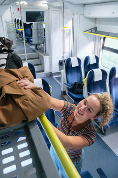 Young woman storing her jacket on the luggage rack in a train