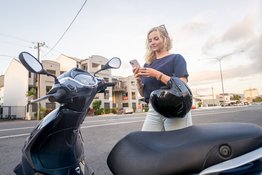 Young Caucasian woman checking her phone before riding her scooter