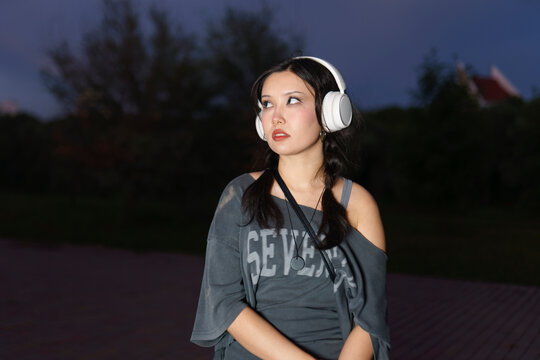 A female listens to music with headphones in the city at sunset