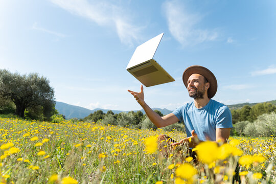 Smiling man throws his laptop in the air in a wildflower field