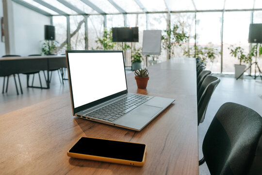 A blank laptop and phone sit on a wooden table in an empty office