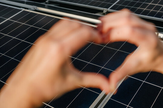Woman forms a heart shape with hands over a solar panel