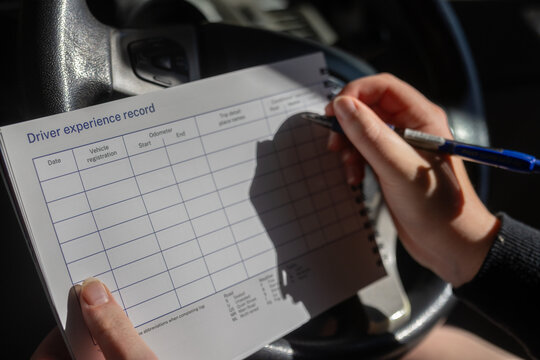 Person sitting in car filling driver experience record logbook using abbreviations