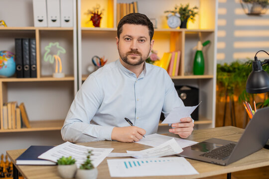 Young man on home table reads contract pages and marks key lines before signature at home. Adult guy on home table carefully checks details in official document and thinks about terms on work laptop.