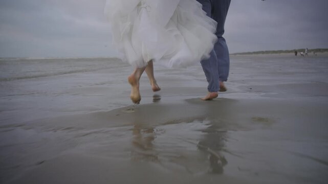 Newlyweds running barefoot on sandy beach rear view