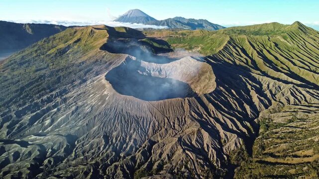 Close drone orbit around the Mount Bromo crater, showcasing intricate volcanic formations and rugged geographical shapes across the crater exterior beneath a vivid blue sky, Indonesia