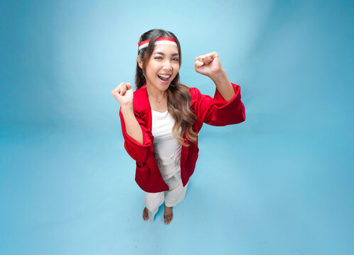 Joyful young Asian woman is raising fists doing celebration gesture.