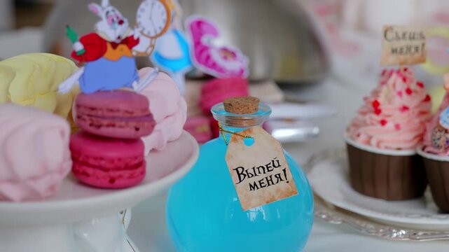 Plate Of Pink Macarons With Blue Potion And Rabbit Topper, Cupcake Frosting With Sprinkles And Pocketwatch Prop, Corked Vial Labeled Playful Storybook Styling, Translation: drink me