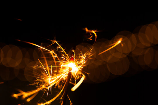 Sparkler glowing with sparks to celebrate new years eve with bokeh lights in background