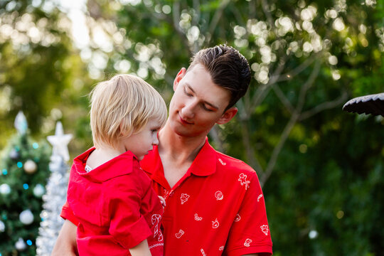 Young dad holding his son wearing matching red Christmas shirts