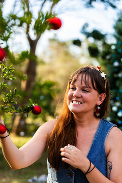 Young woman in her twenties hanging red baubles on tree outside