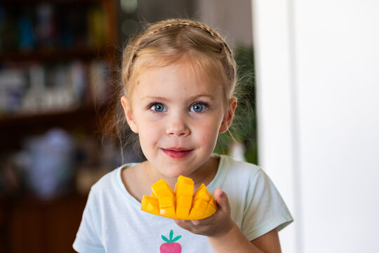 Little Australian girl eating a freshly cut mango fruit in kitchen at home