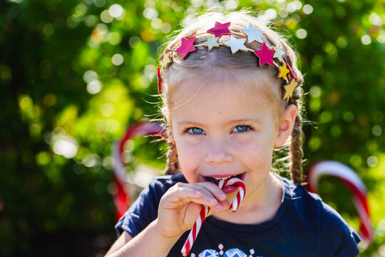 Happy little girl eating red and white striped candy cane at Christmas outdoors