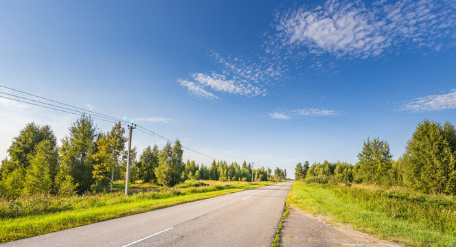 Gravel road flanked by greenery under clear blue sky with wispy clouds