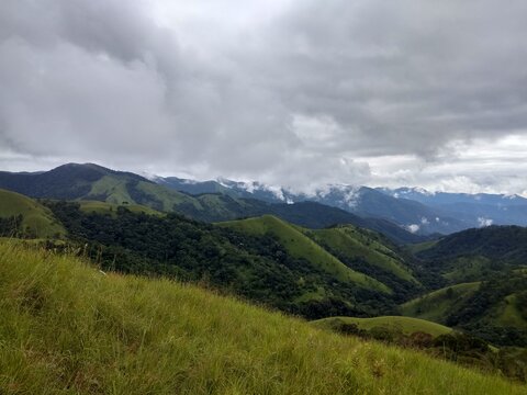 Lush Green Rolling Hills and Mountains Under Cloudy Sky