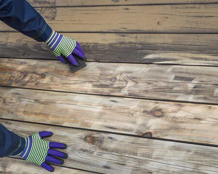 Person sands old wood deck wearing striped gloves