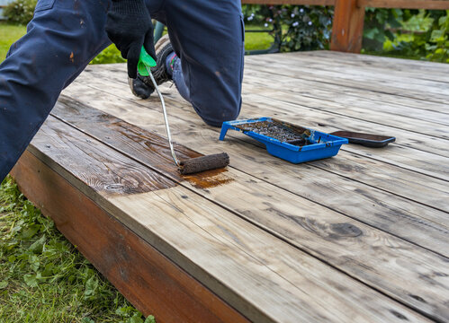 Worker applies wood stain to deck with roller