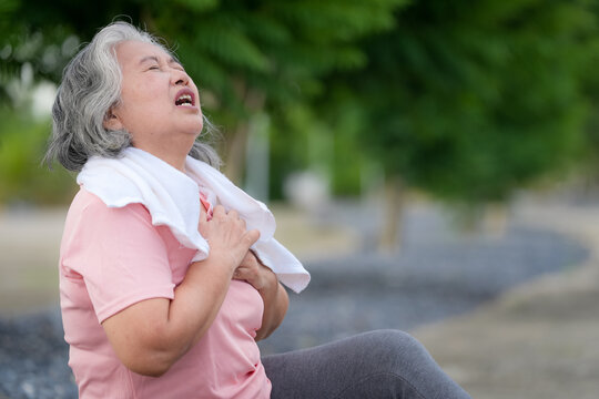 Senior woman chest pain breathlessness heart health exercise outdoor, sitting on path with towel, clutching chest after workout, medical emergency concept, copy space