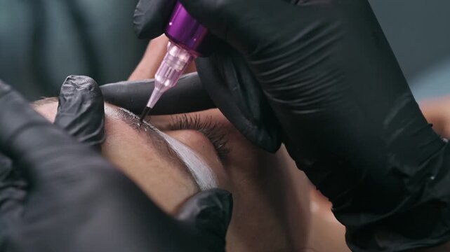 Close up of a permanent makeup machine creating an eyebrow tattoo during a PMU procedure in a professional beauty salon with precise cosmetic pigmentation.