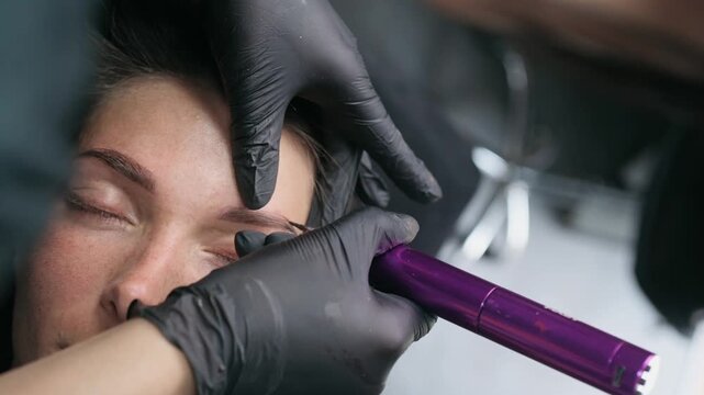Permanent makeup artist applies white mapping paste to outline eyebrow shape before a cosmetic tattoo procedure in a professional beauty studio.