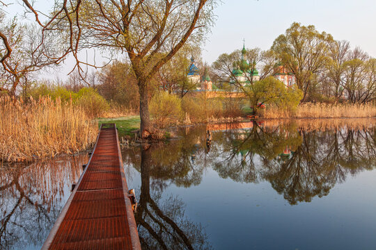 Beautiful scenic view of a forest lake with a footbridge and historic orthodox monastery reflection at sunset