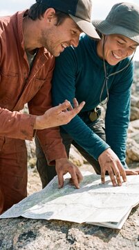 Engaged hikers laughing while pointing at folded trail map close up outdoors