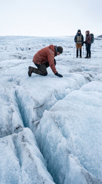 Focused climber examining deep glacier crevasse while companions observe nearby