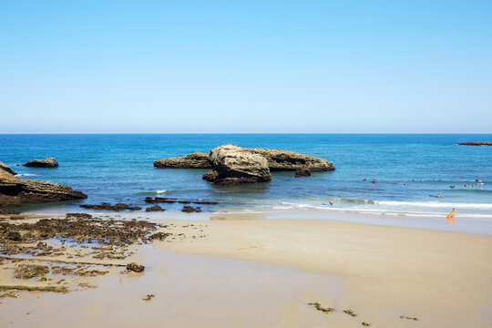 Scenic View of Coastal Rock Formations, Sandy Shore, and Surfers in the Sea at Biarritz, France