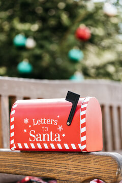 Red Christmas mailbox for letters to Santa on rustic wooden bench with decorated Christmas tree in background. Christmas and New Year traditions to order gifts by mail from Santa