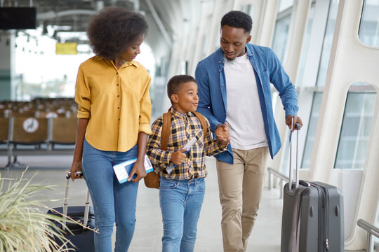 A smiling family of three, parents and son, are walking together in an airport terminal with their suitcases and travel documents