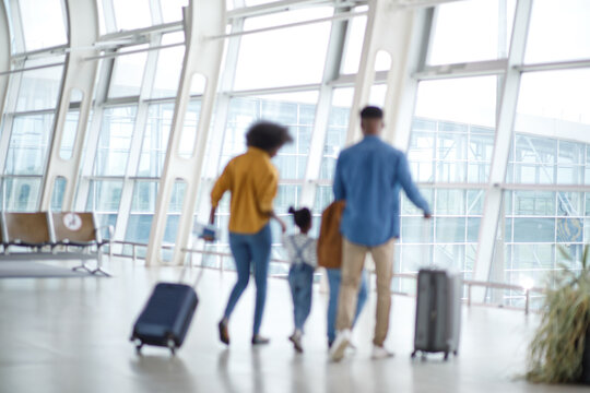 A family of four, including two children, walks through a bright, contemporary airport concourse with suitcases in tow