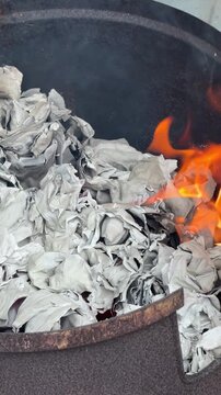 Vertical 4K alternative close up angle of gold joss paper burning into embers inside metal container. 