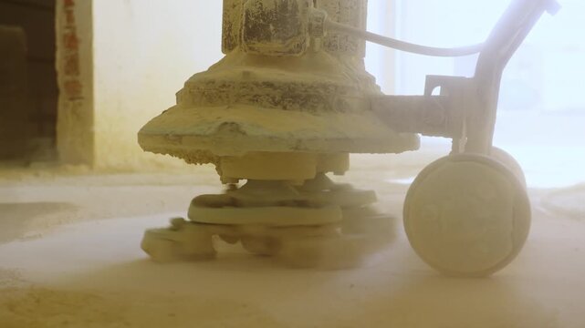 Heavy floor grinding machine polishing dusty concrete surface. Concrete dust coats equipment base and wheels during grinding process