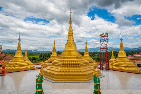 Pyitha Line Aye Pagoda, also known as Phra That Tagaw, features golden stupas on a wide open courtyard with green naga balustrades under a cloudy sky in Kayin State, Myanmar.