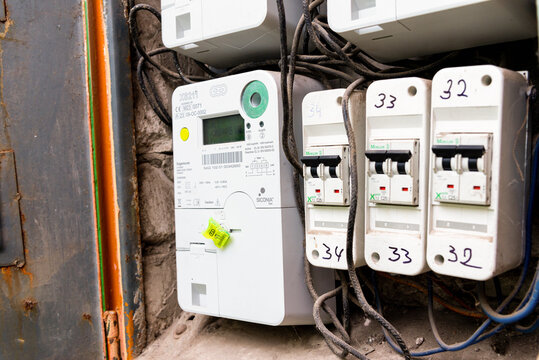 Old digital electric meter and circuit breaker mounted on a weathered industrial panel with rusty metal structures, showing energy usage measurement and vintage wiring. Telsiai, Lithuania 08-26-2026