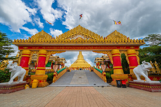 Pyay Tha Lin Aye Pagoda, also known as Phra That Tagaw, features a golden stupa, ornate entrance arch, red pillars, and white elephant statues under a blue sky in Kayin State, Myanmar.
