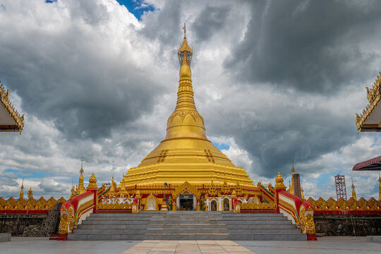 Pyay Tha Lin Aye Pagoda, known as Phra That Tagaw, features a majestic golden stupa under dramatic cloudy skies, framed by ornate staircases in Kayin State, Myanmar.