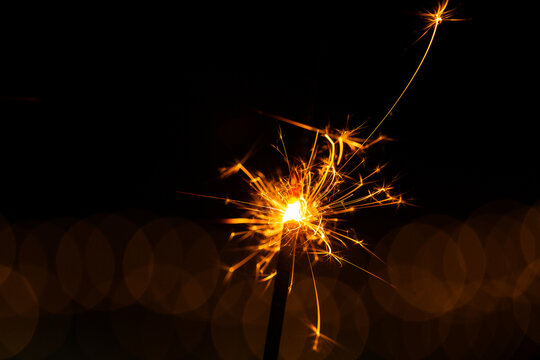 Sparkler glowing with sparks to celebrate new years eve with bokeh lights in background