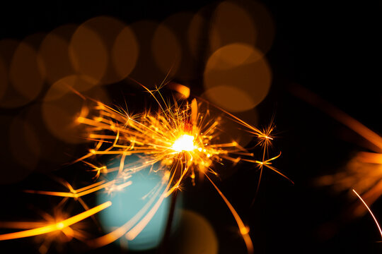Sparkler glowing with sparks to celebrate new years eve with bokeh lights in background