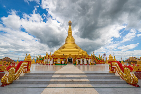 Pyay Tha Lin Aye Pagoda, known as Phra That Tagaw, features a majestic golden stupa centered in a spacious courtyard under dynamic cloudy sky in Kayin State, Myanmar.