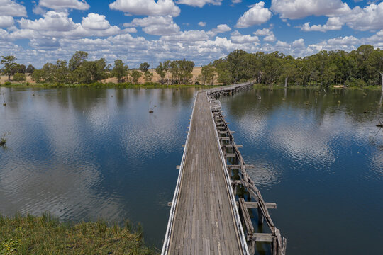 Aerial view over a abandoned wooden bridge over a calm river with cloud reflections
