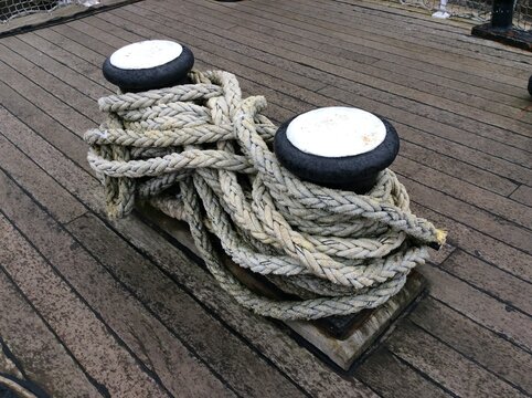 Heavy maritime ropes coiled around black and white deck fittings on a weathered wooden vessel deck.
